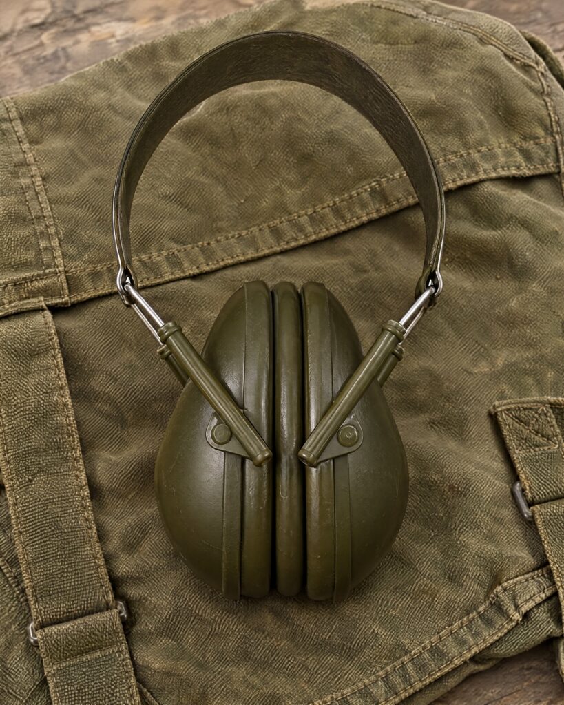 Olive-green folding ear defenders with stainless-steel headband on canvas