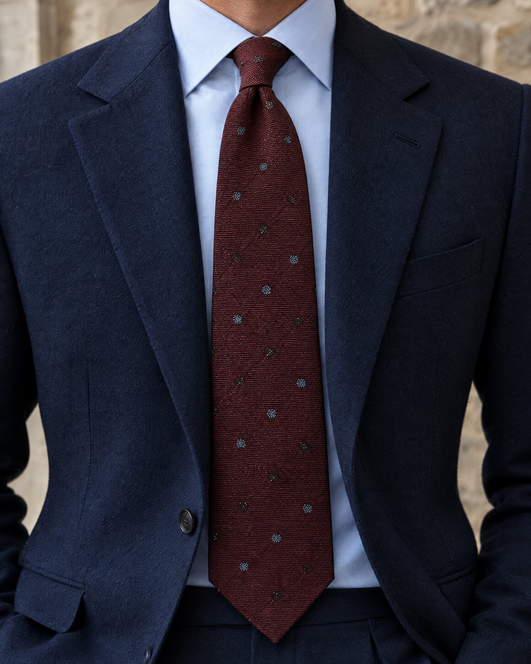 Man in navy suit and pale blue shirt wearing a wide burgundy silk tie, cropped at the chin