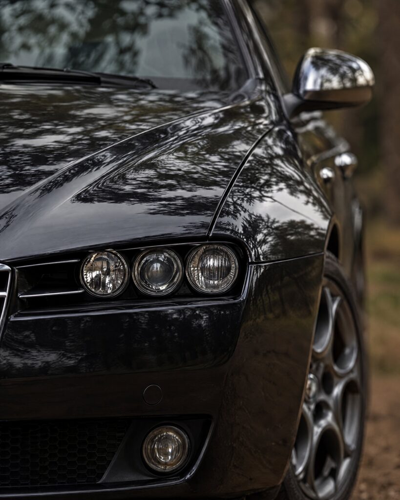 Close detail of the headlamp cluster and sculpted bonnet of a black Alfa Romeo 159 saloon