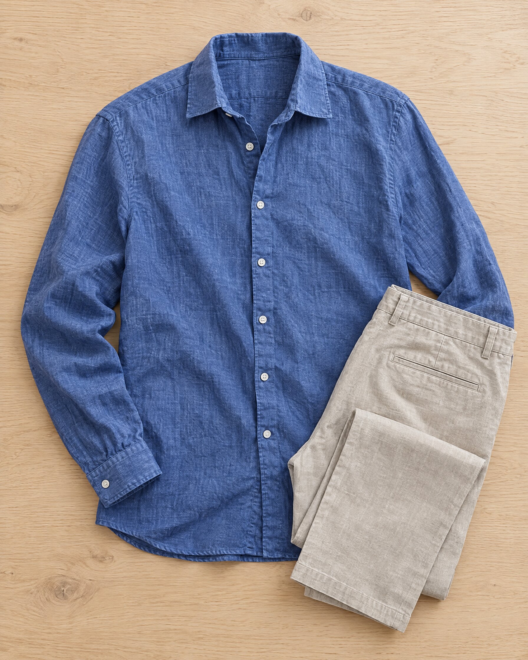Indigo blue linen shirt laid flat beside stone trousers on oak
