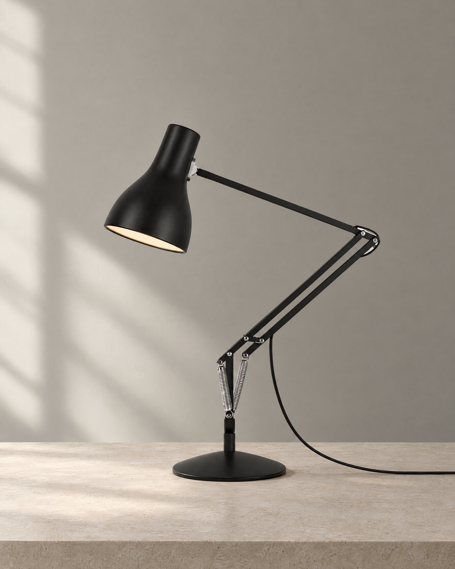Anglepoise Type 75 desk lamp in Jet Black on a pale stone surface in soft natural light
