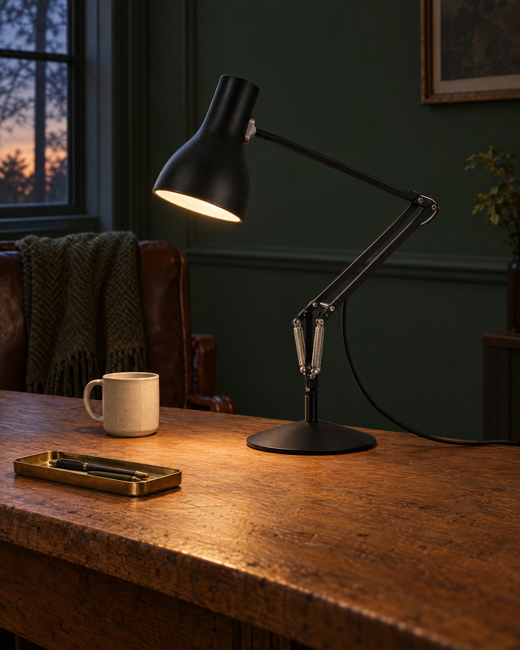 Black Type 75 task lamp lit over an oak desk in a quiet study at dusk