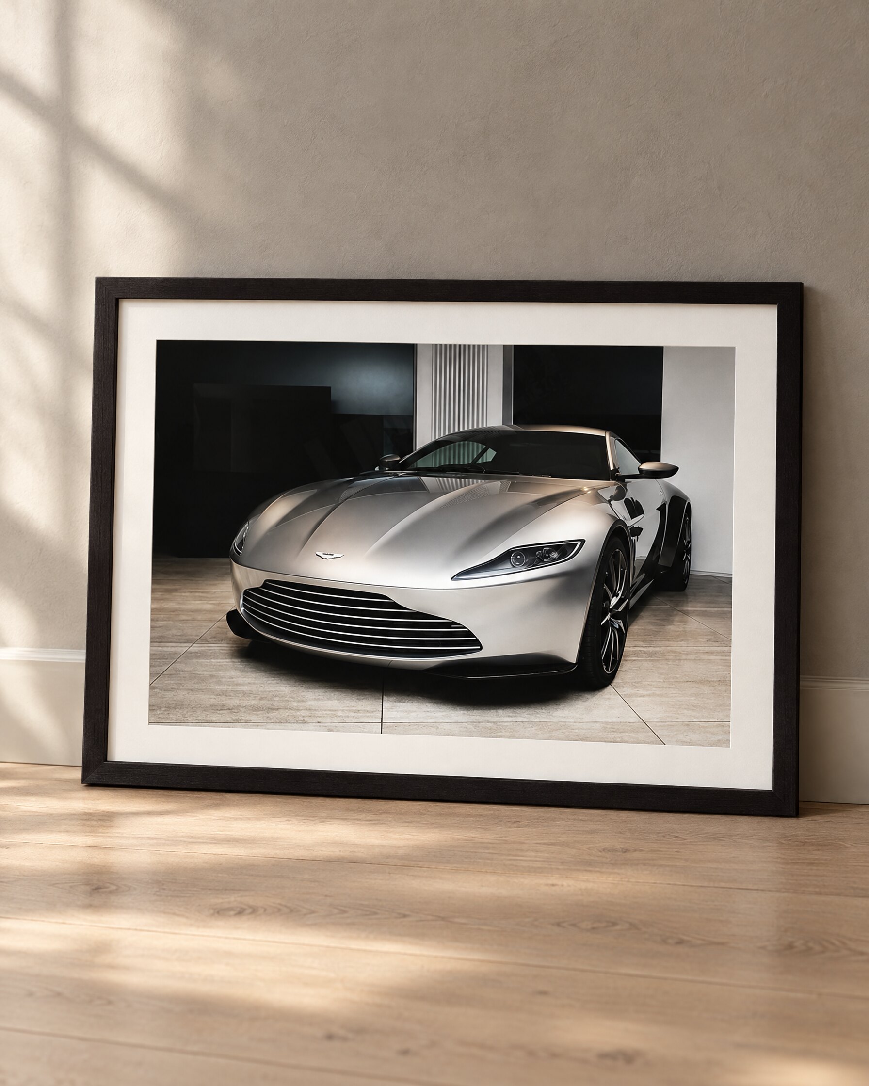 Framed Aston Martin DB10 print leaning against a grey plaster wall