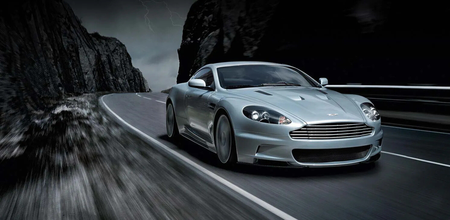 Dark grey Aston Martin DBS Quantum of Solace car parked on a quiet Italian lakeside road at dawn