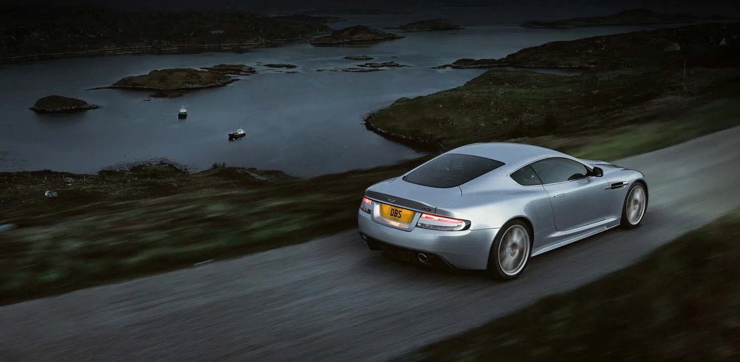Dark grey Aston Martin DBS Quantum of Solace car parked on a quiet Italian lakeside road at dawn