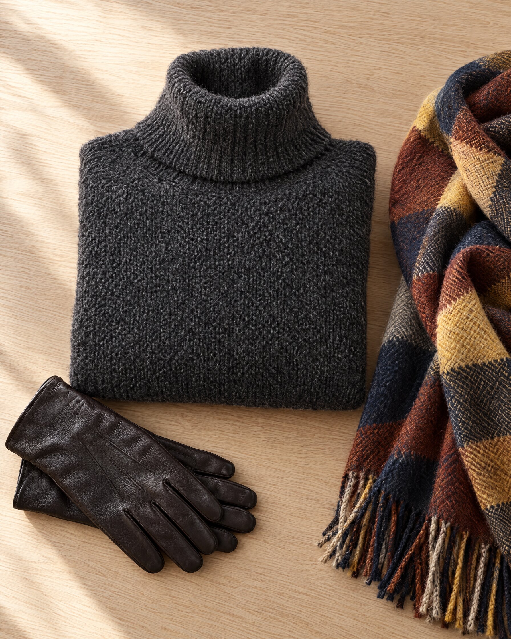 Charcoal grey chunky cashmere turtleneck sweater folded on an oak table