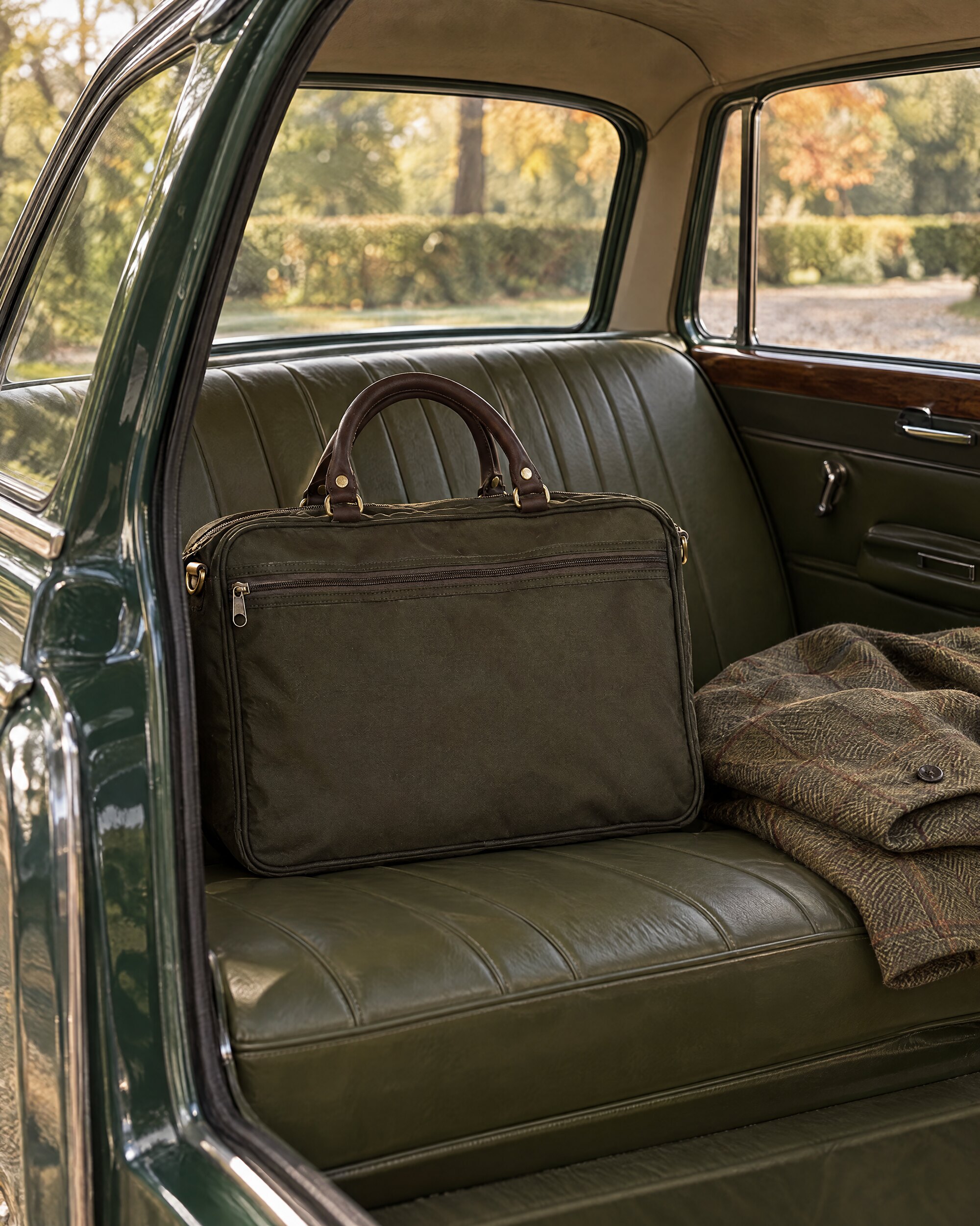 Olive leather-trimmed briefcase on the back seat of an estate car beside a folded tweed jacket