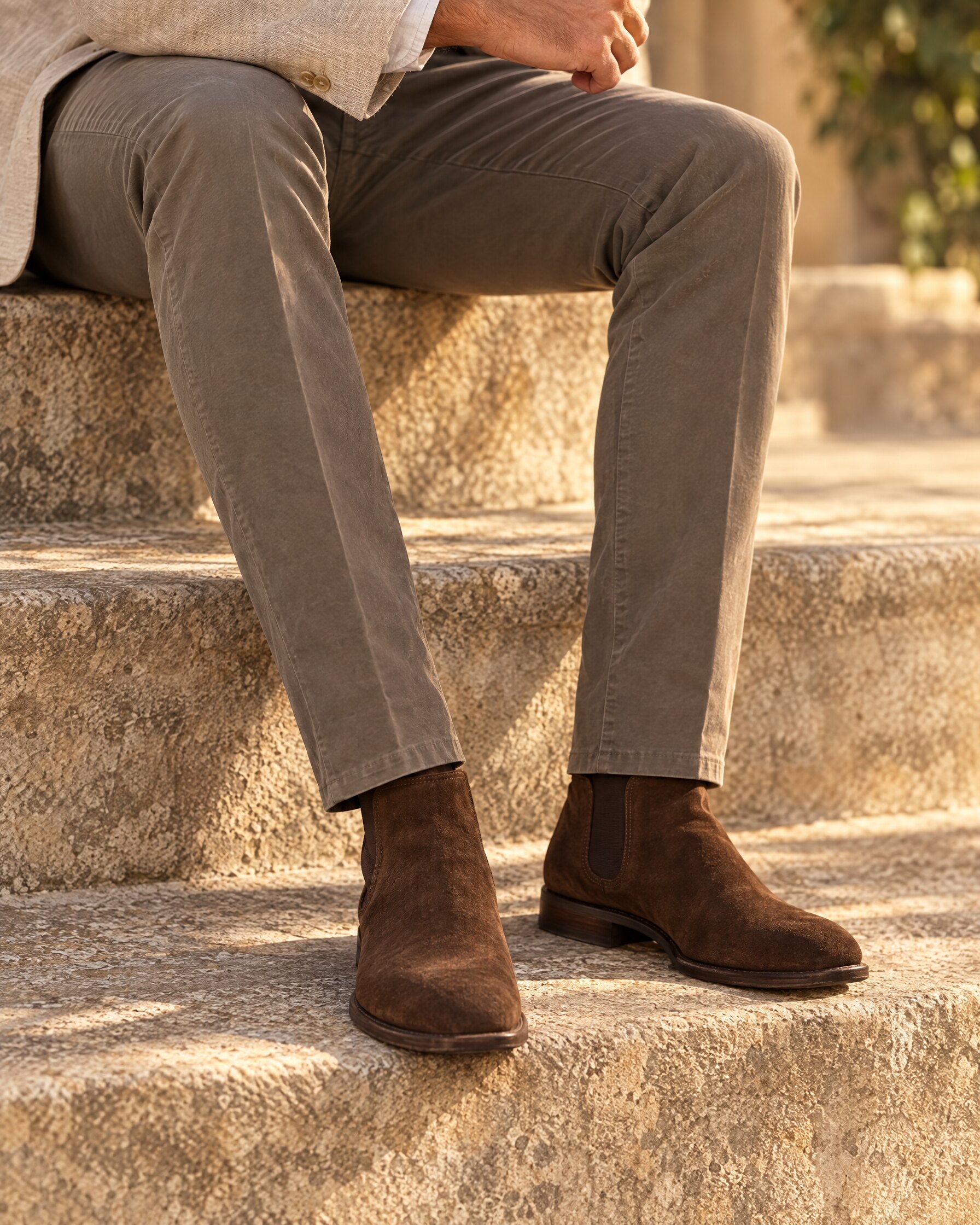 Man in Brunello Cucinelli Spectre chinos style dark khaki gabardine trousers and brown suede boots on a stone step