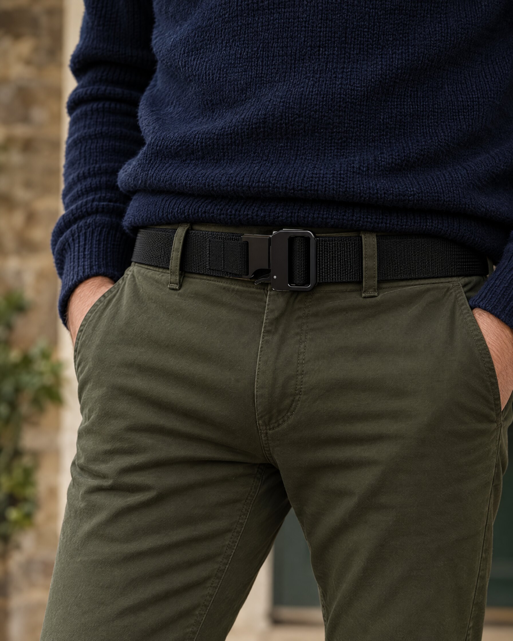 Black webbing belt with matte black quick-release buckle worn with olive chinos and a navy knit