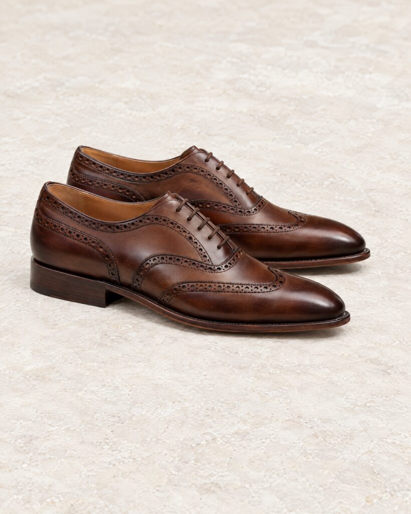 Walnut-brown full brogue Oxford shoes with perforated toe caps on a stone surface