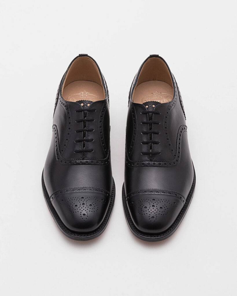 Black calf Oxford semi-brogues on a pale stone floor, the Church's Diplomat style