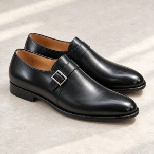 Black single-strap monk shoes with a plain toe on a stone surface