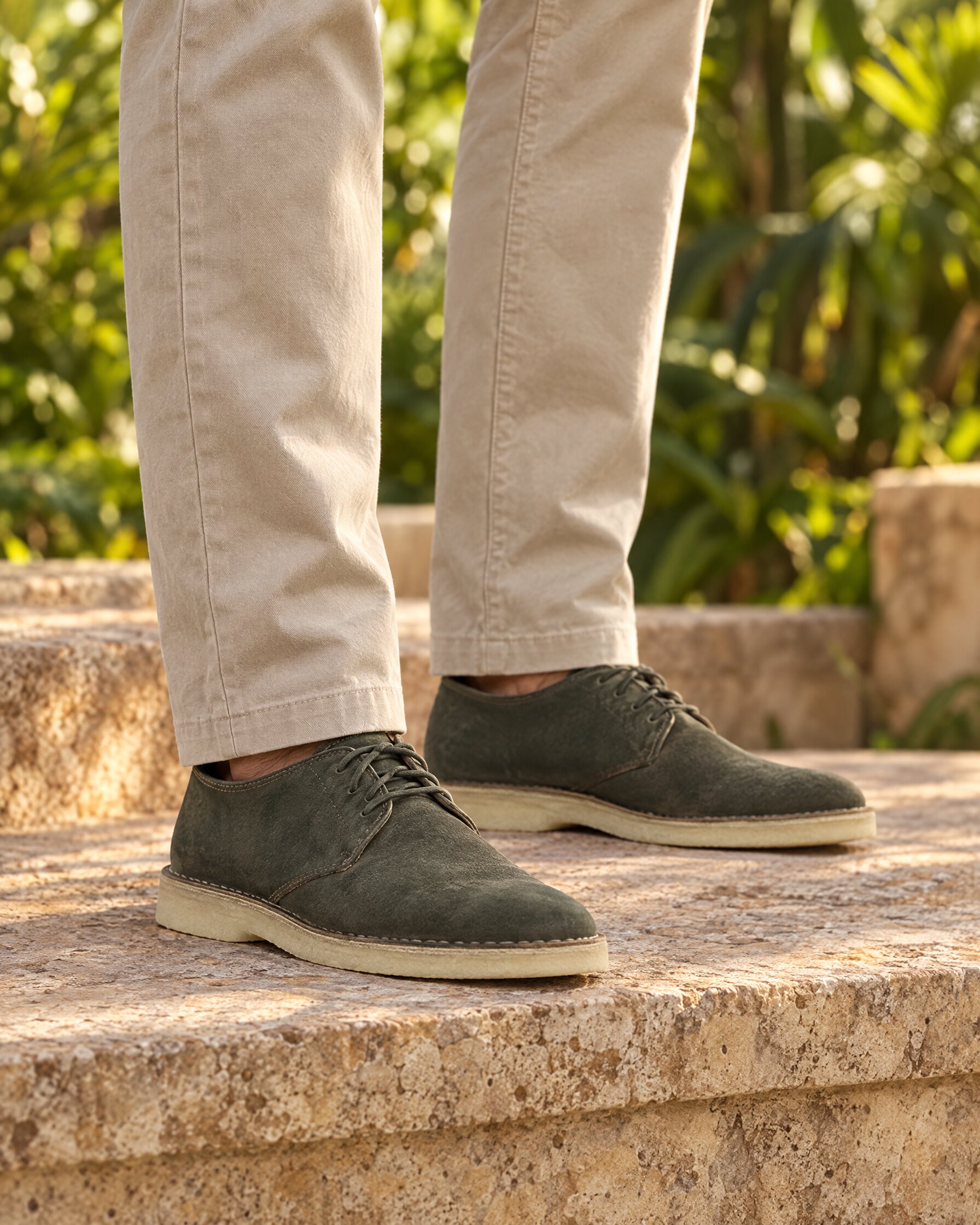Man's feet in pine green suede lace-up shoes with crepe soles on a stone terrace