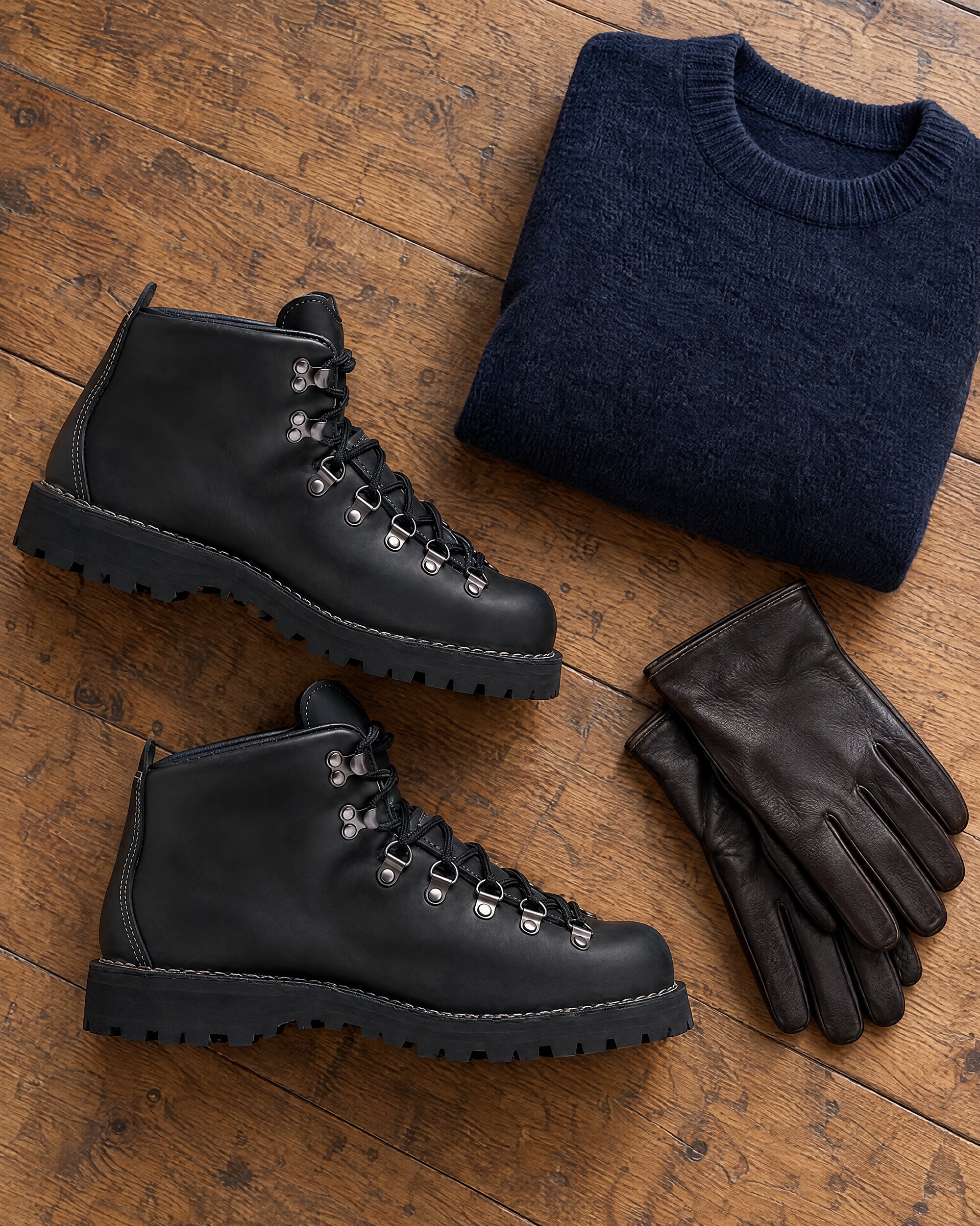 Danner Mountain Light II black boots on an oak floor beside a folded navy wool jumper