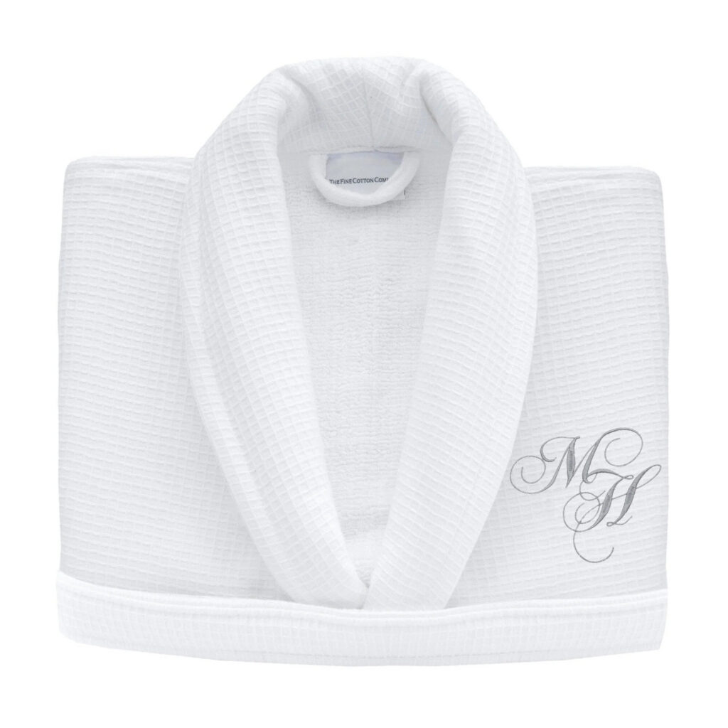 Folded cotton bath towels with a dark green border on an oak bench, in the style of a Fine Cotton Company embroidered towel