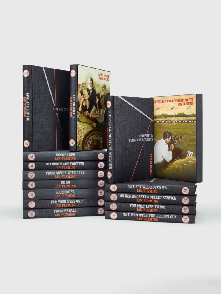 Dark cloth-bound hardback beside an illustrated slipcase on a wooden desk