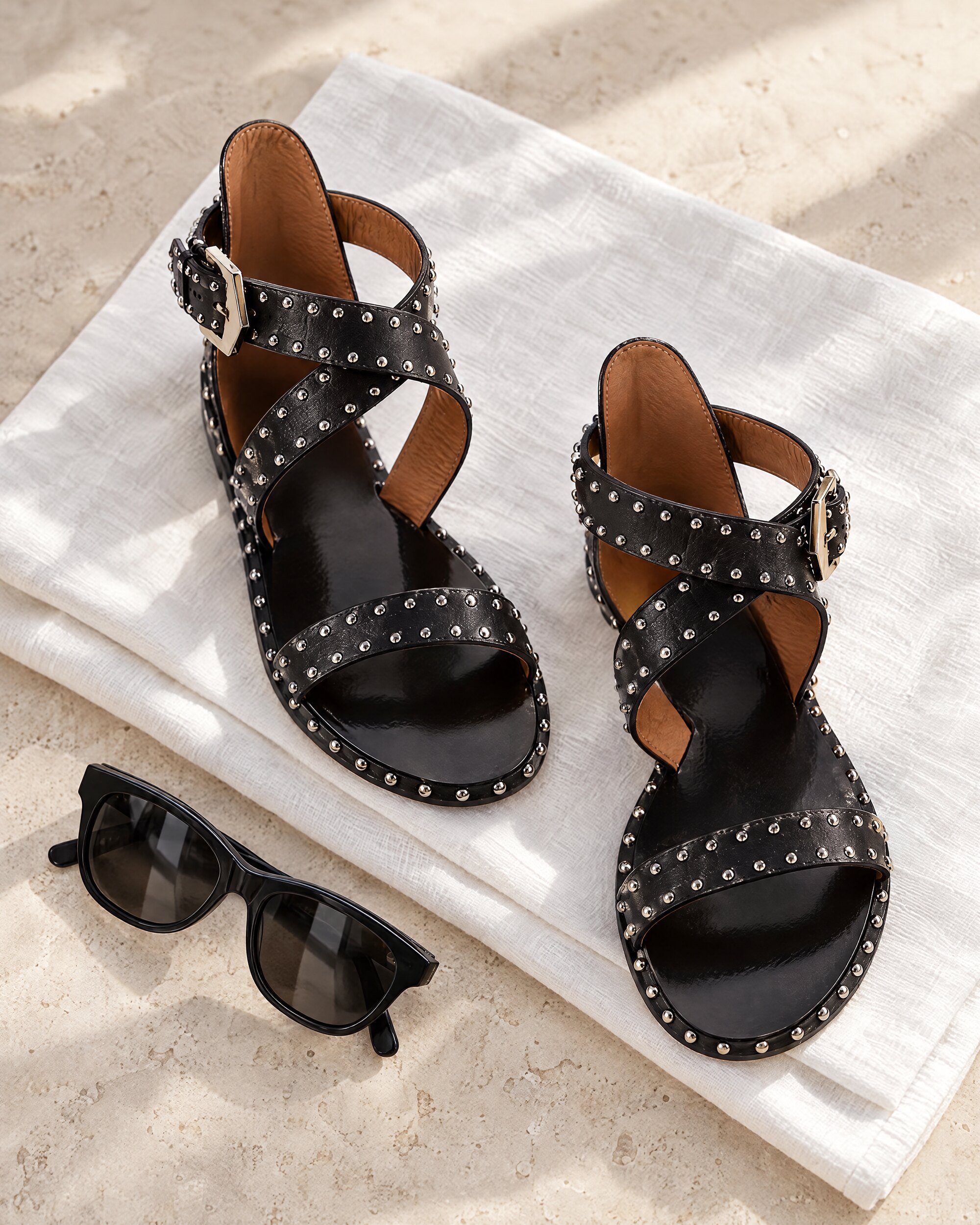 Givenchy Elegant studded sandals in black calfskin with silver studs and a crisscross ankle strap, laid on white linen