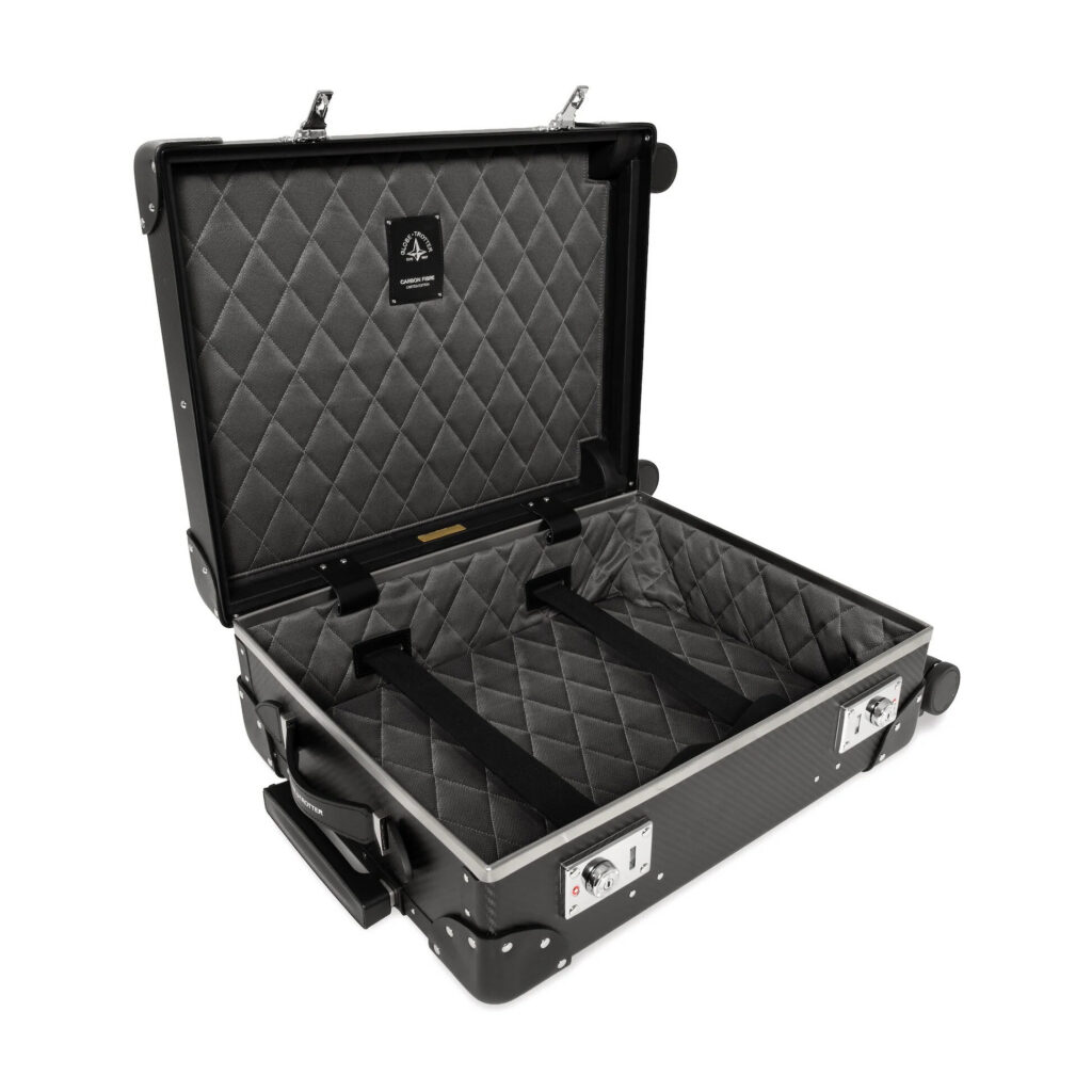 Graphite carbon fibre four-wheel carry-on case standing on a limestone floor in soft natural light