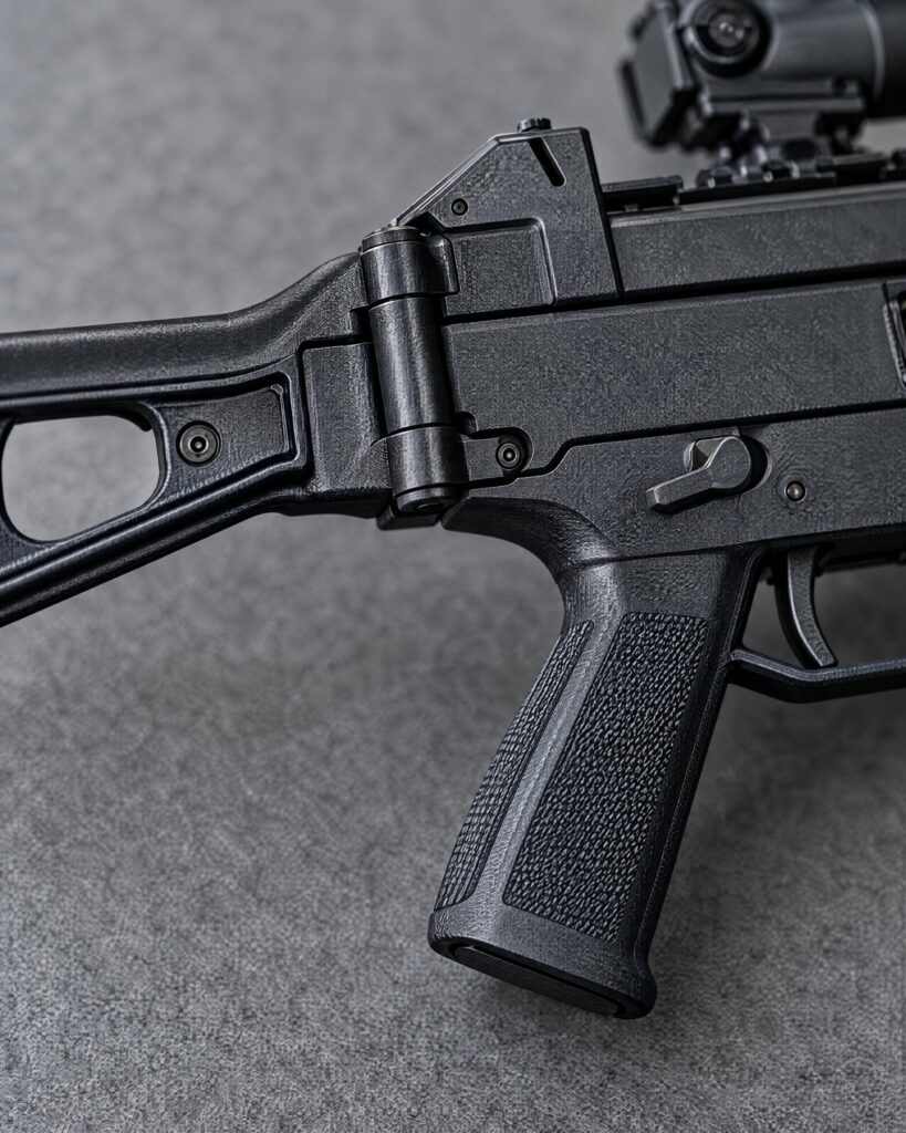 Detail of the polymer grip and folding stock hinge of a Heckler & Koch UMP-9 style submachine gun