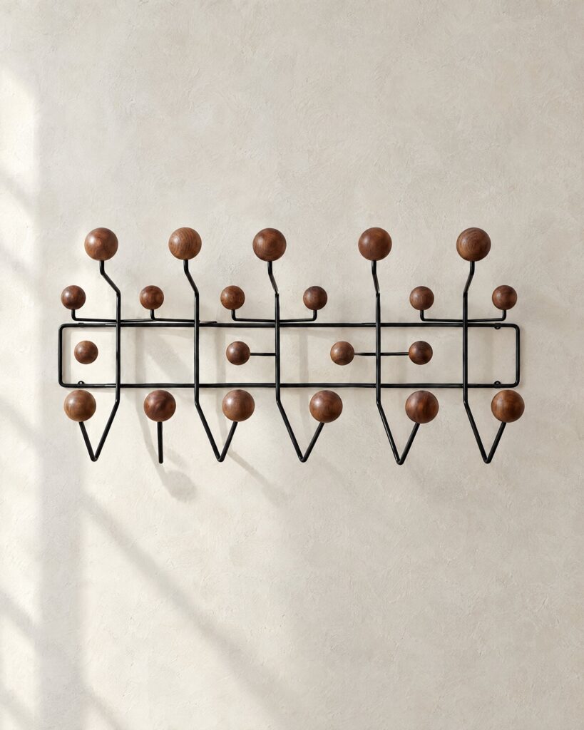 Eames Hang-It-All wall rack in black steel with walnut knobs on a pale plaster wall