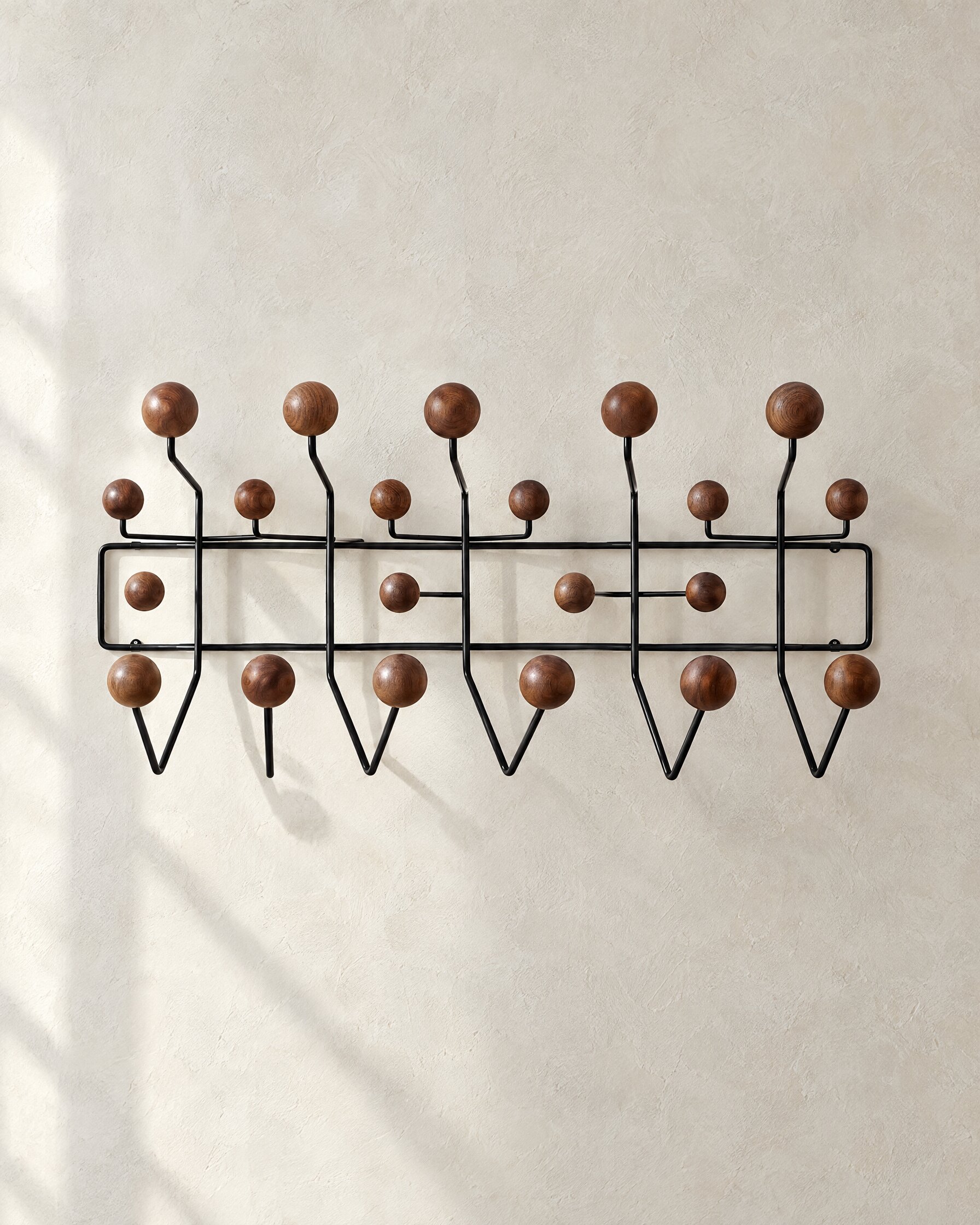 Eames Hang-It-All wall rack in black steel with walnut knobs on a pale plaster wall