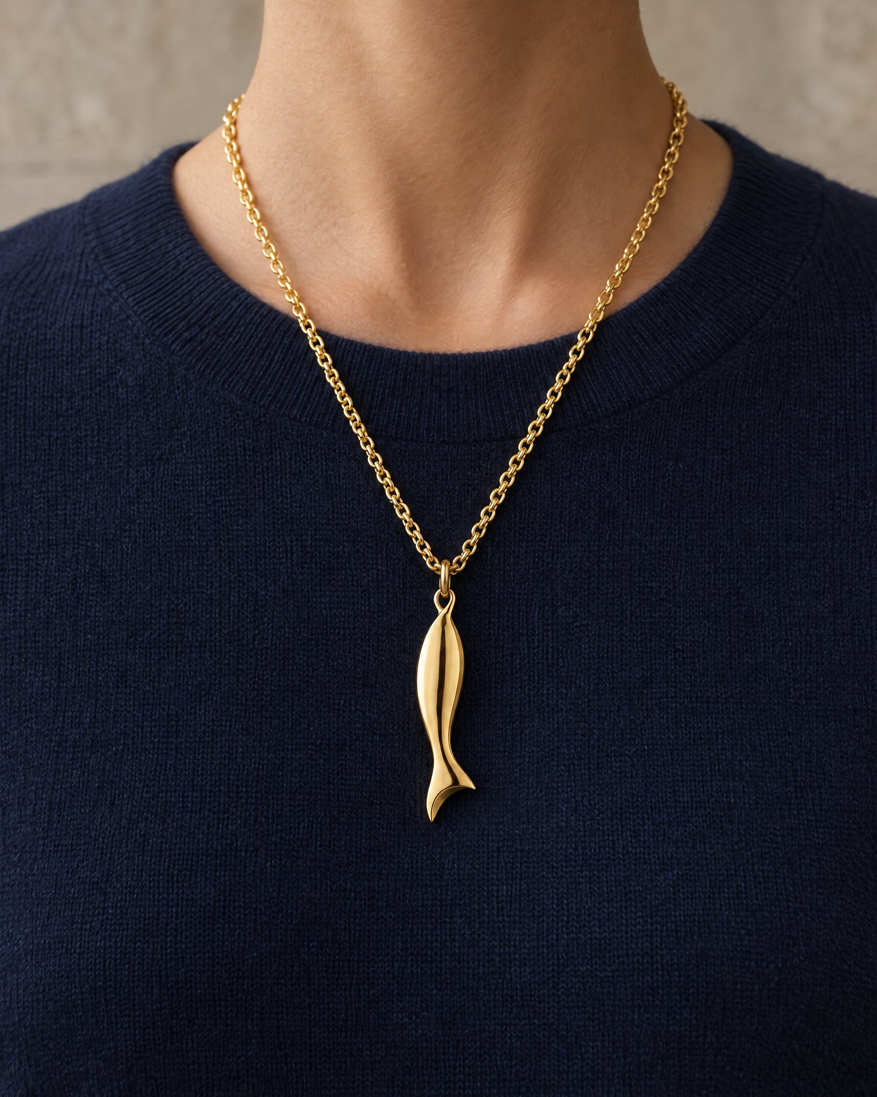 Gold chain necklace with fish pendant worn over a navy knit