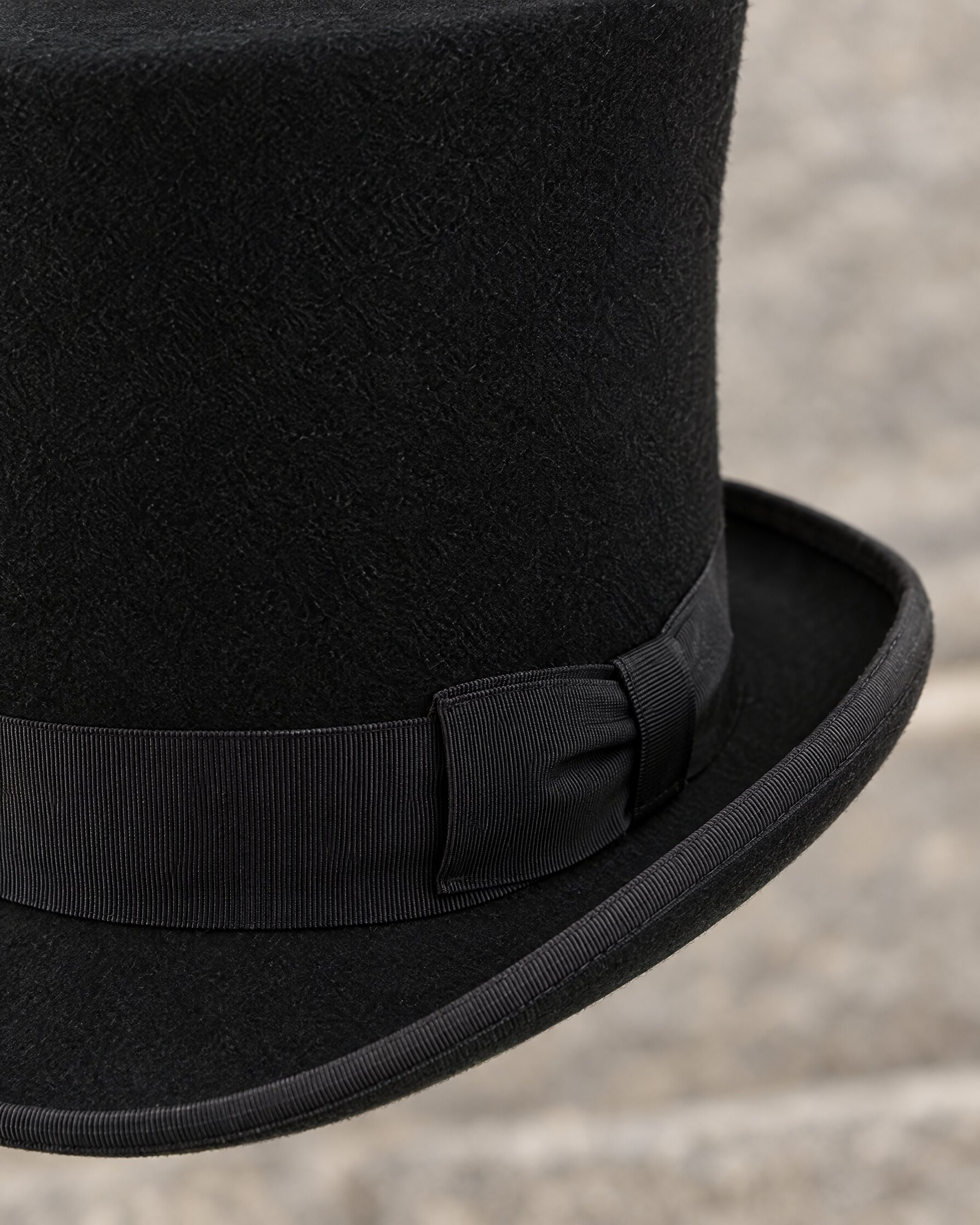 Close detail of the ribbon-bound curled brim on a black wool felt Victorian top hat
