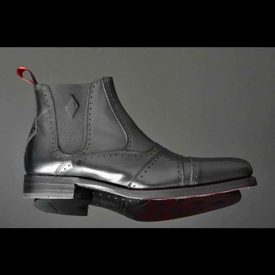 Brown brogue Chelsea boots with red lining on a stone floor