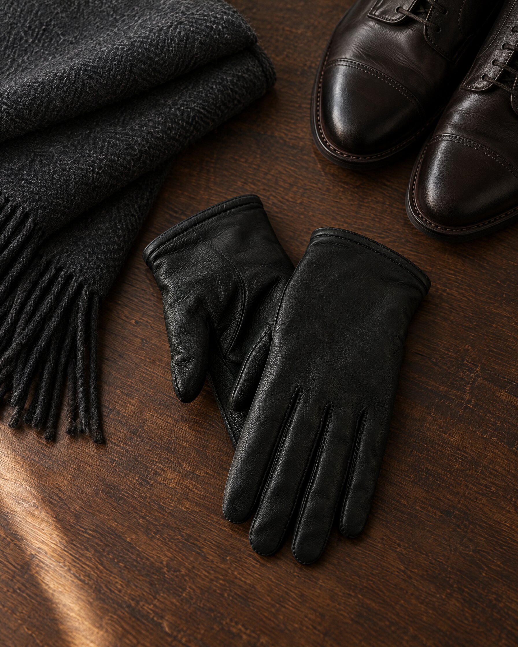 Black deerskin gloves in the style of the Mulberry Day Glove laid flat with a charcoal scarf on dark oak
