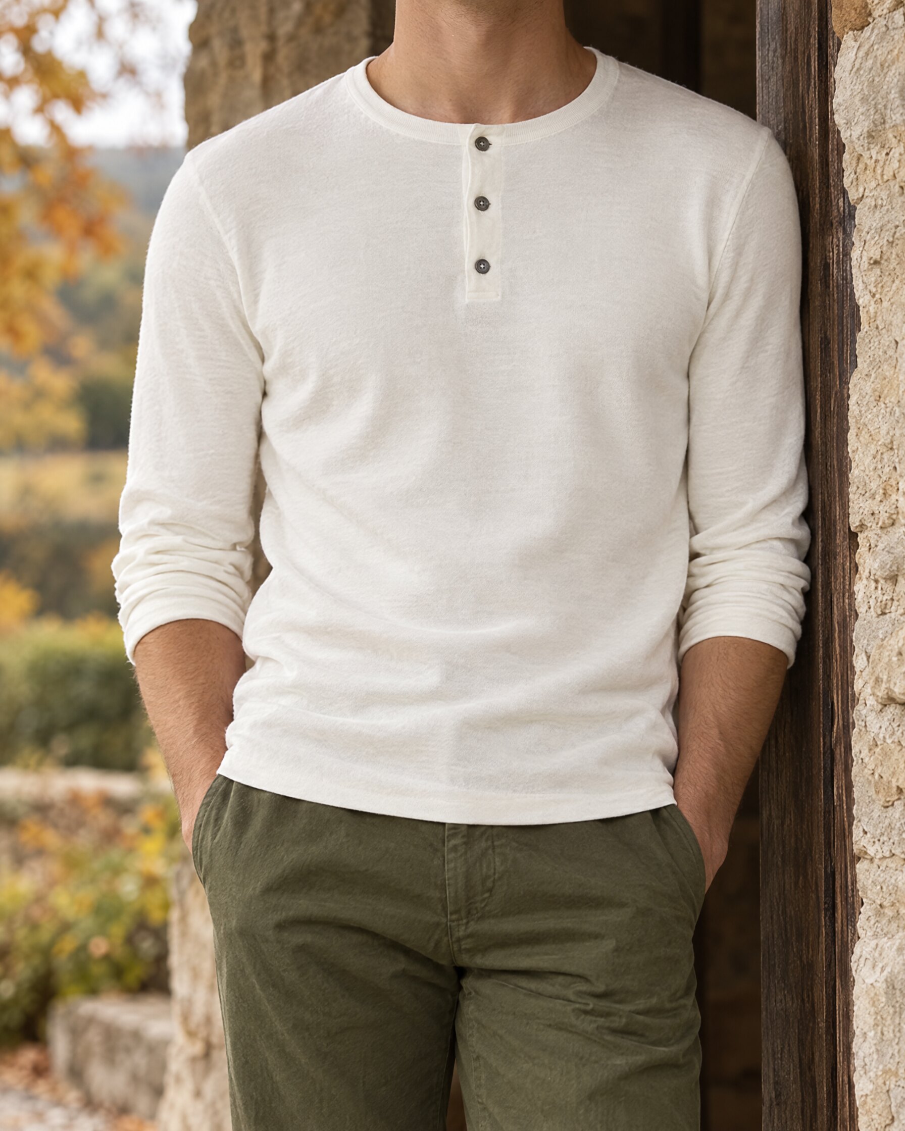 Man wearing the N.Peal 007 Henley in ivory white with olive trousers in a stone doorway