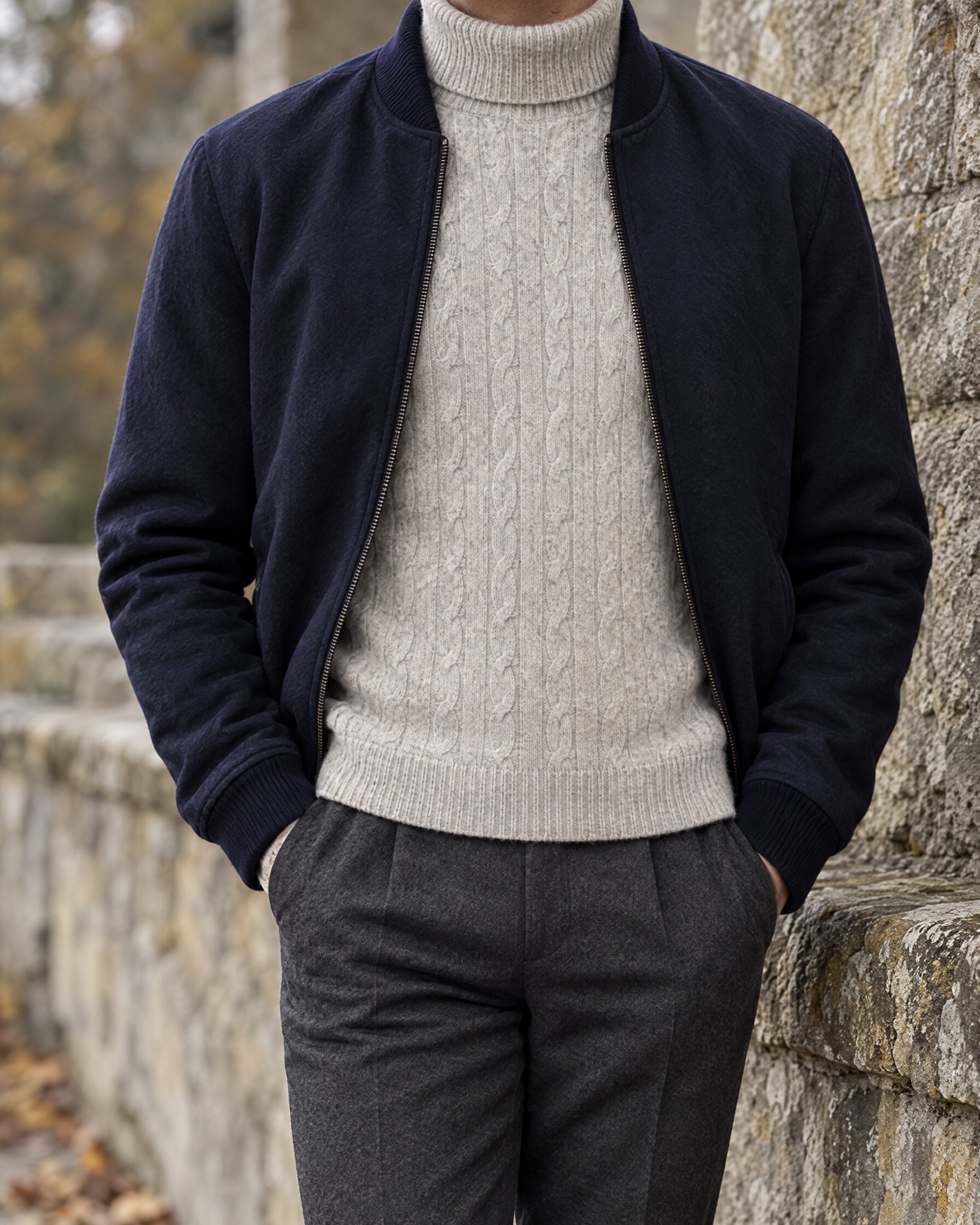 Man wearing the N.Peal cable roll neck sweater in Fumo Grey under a navy bomber jacket