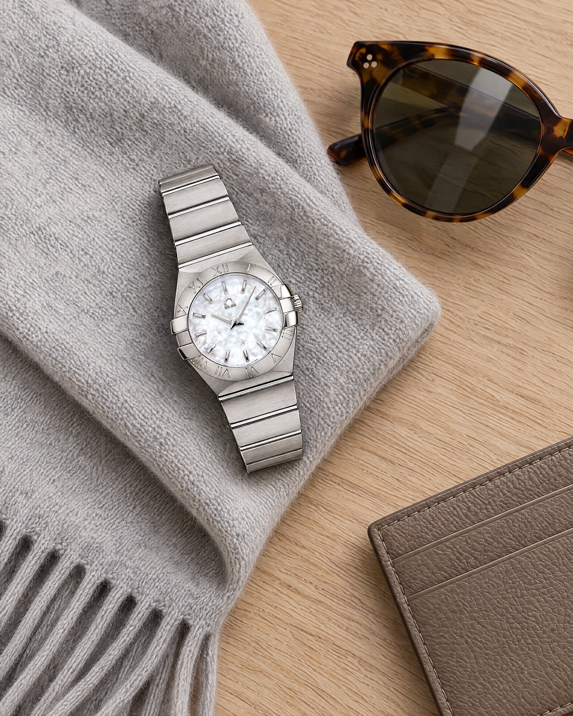 Omega Constellation Quartz 27mm in brushed steel with mother-of-pearl dial, laid on grey cashmere beside sunglasses
