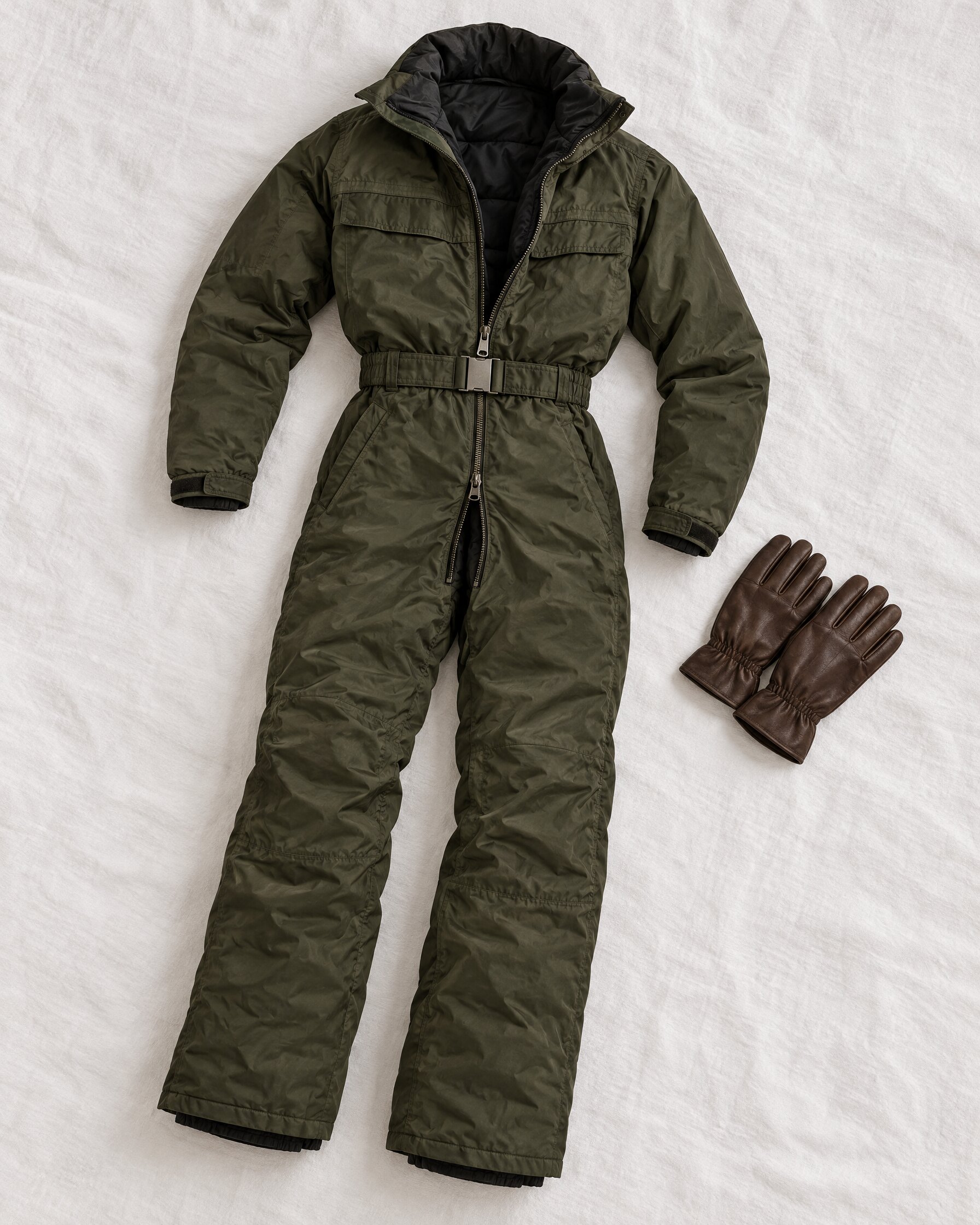 Dark olive one-piece ski suit with belt laid flat beside leather gloves