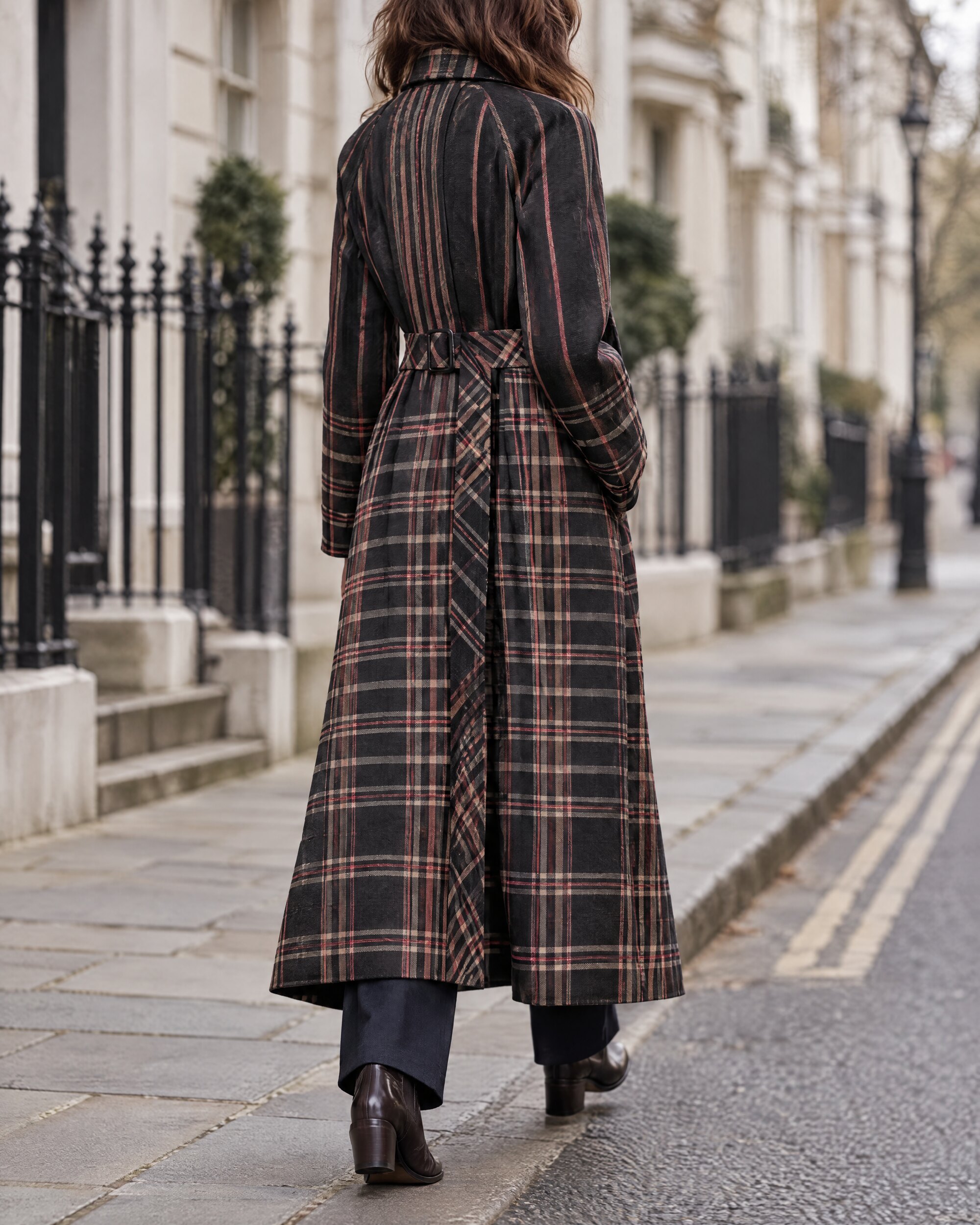 Woman in a long black check mac coat belted at the waist, walking along a quiet London street