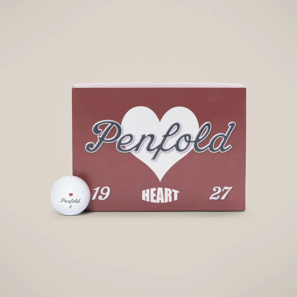 White golf balls with a red heart marking on short turf