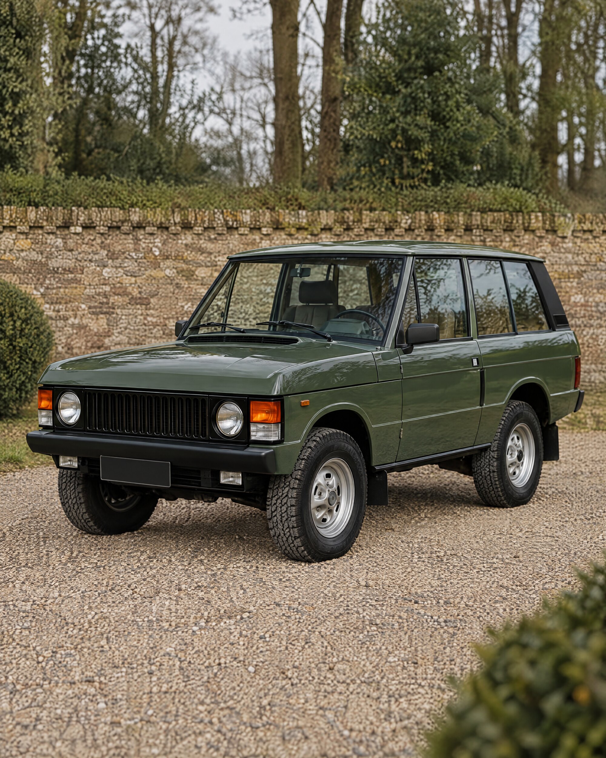 Front corner of a green first-generation Range Rover Classic on a gravel drive