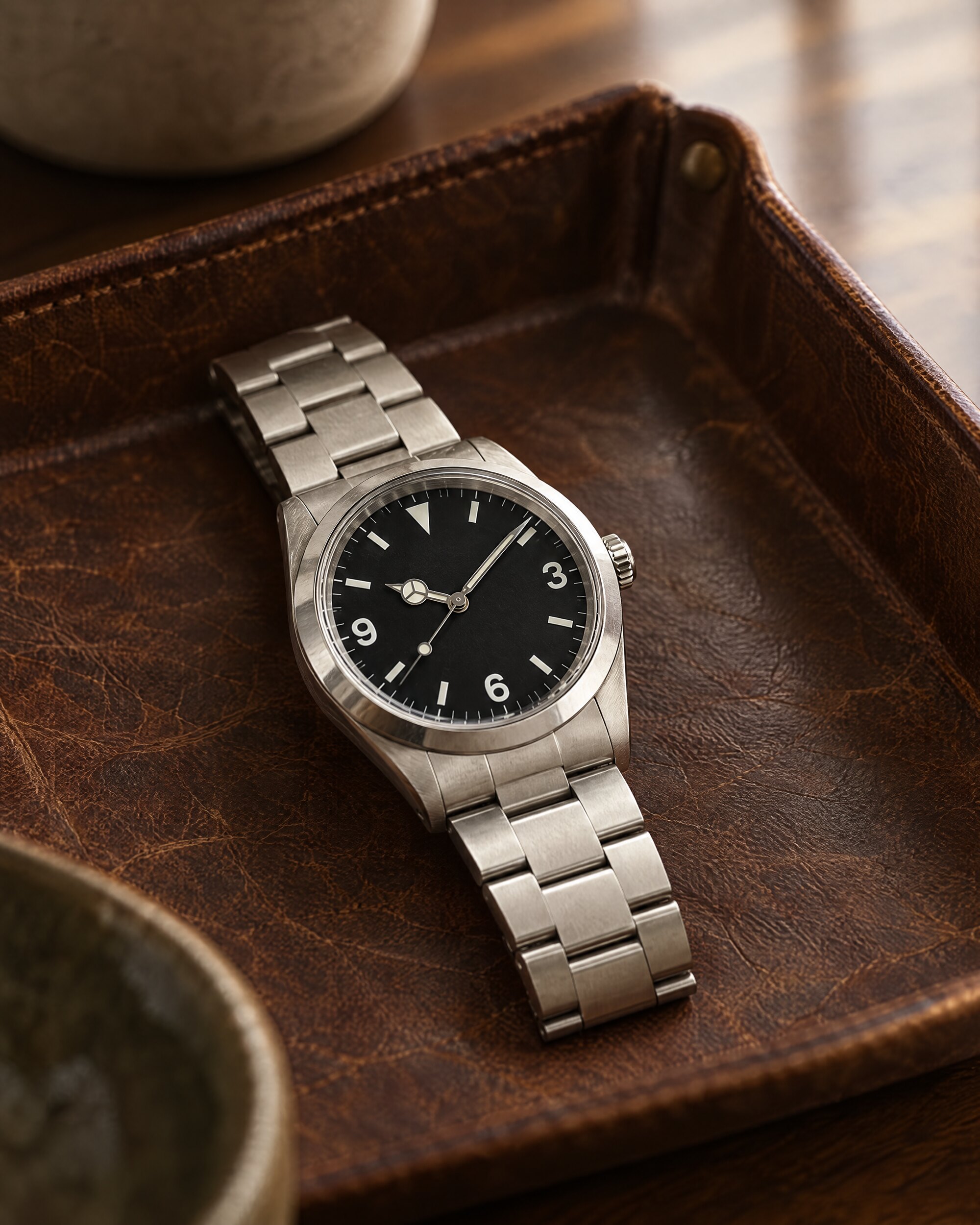 Steel 36mm watch with a black dial and Arabic numerals at 3, 6 and 9 on a leather tray, in the style of the Rolex Explorer 1016