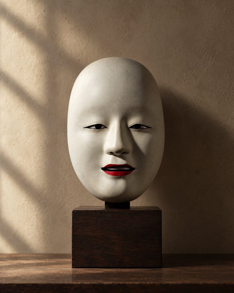 Safin mask replica, a white Noh-inspired mask, on a dark wooden plinth against a plaster wall