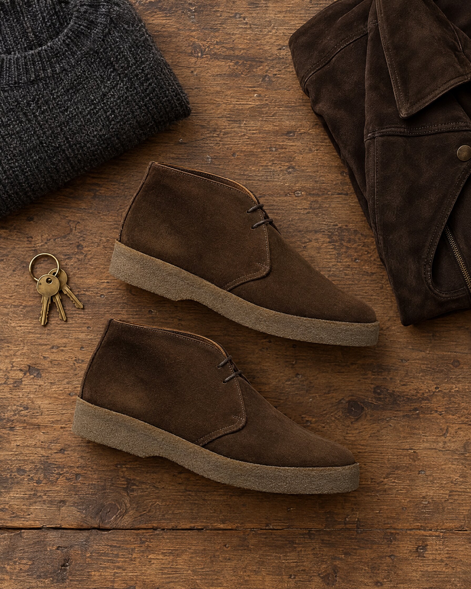 Sanders Hi-Top chukka boot in chocolate suede with crepe sole, laid flat beside a charcoal knit and suede jacket