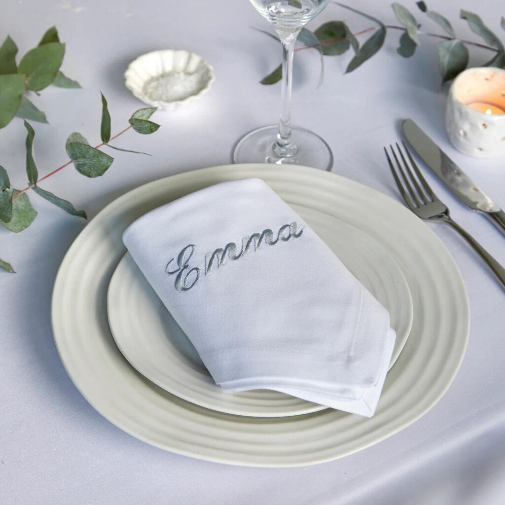 Folded white cotton napkin on a white plate, in the style of the Spectre embroidered napkins