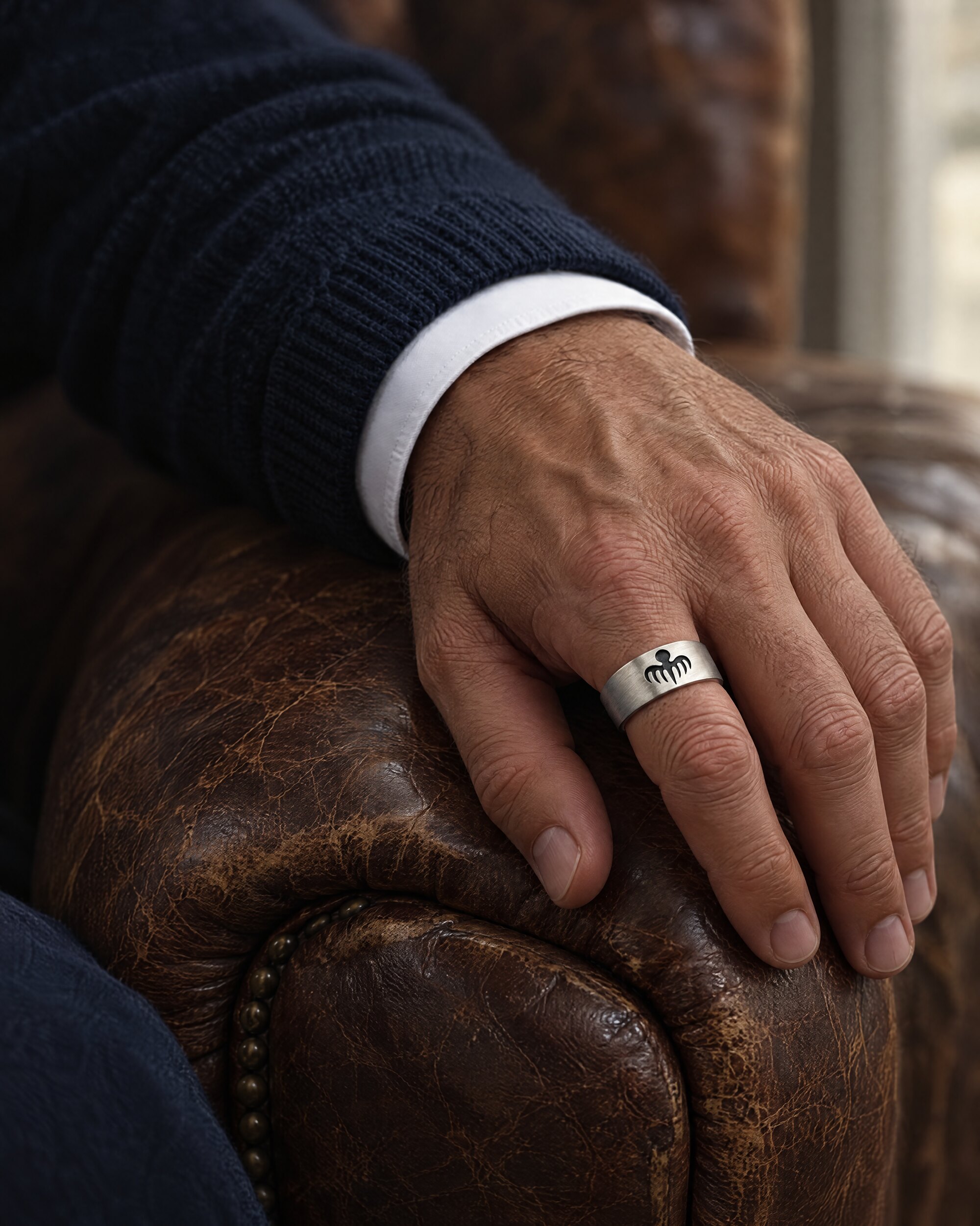Sterling silver octopus ring worn on the little finger of a man's left hand against a leather armchair
