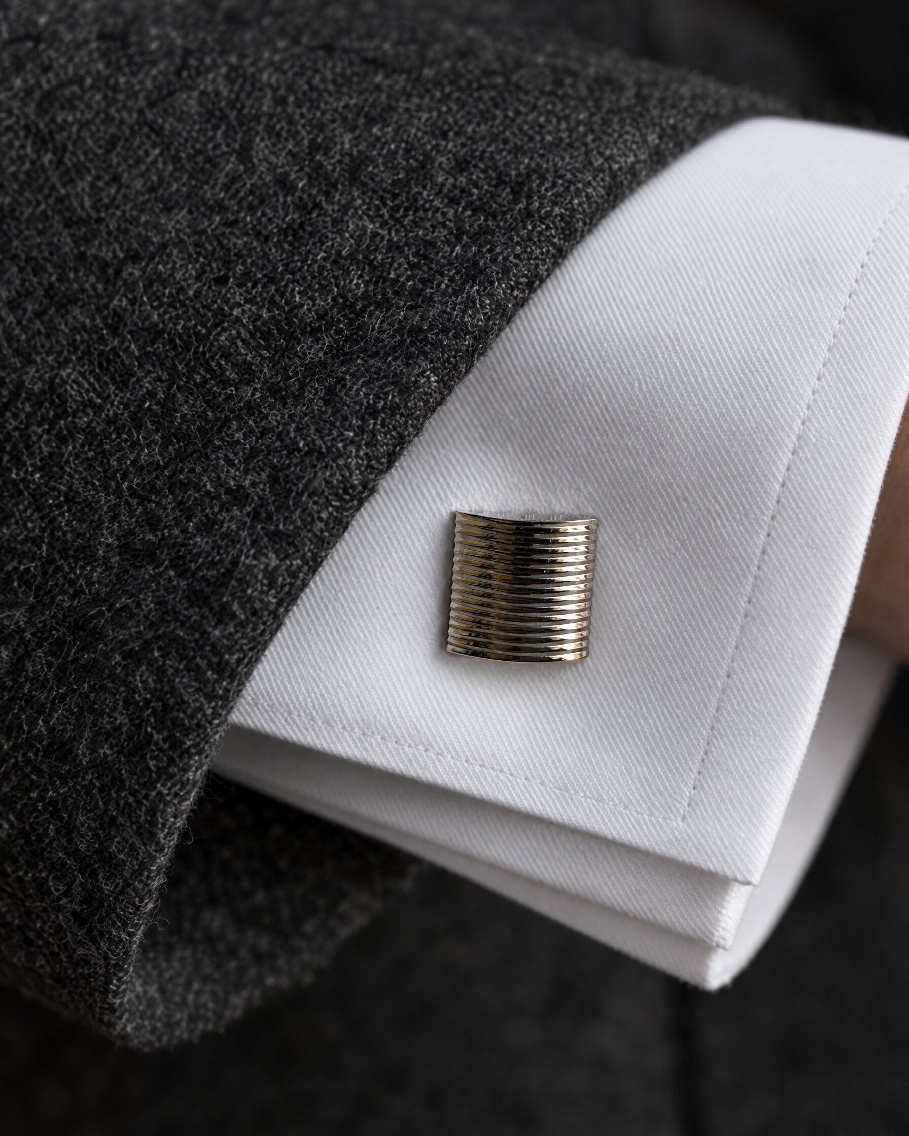 Close-up of a square palladium cufflink fastened through a white double cuff beneath a charcoal flannel sleeve