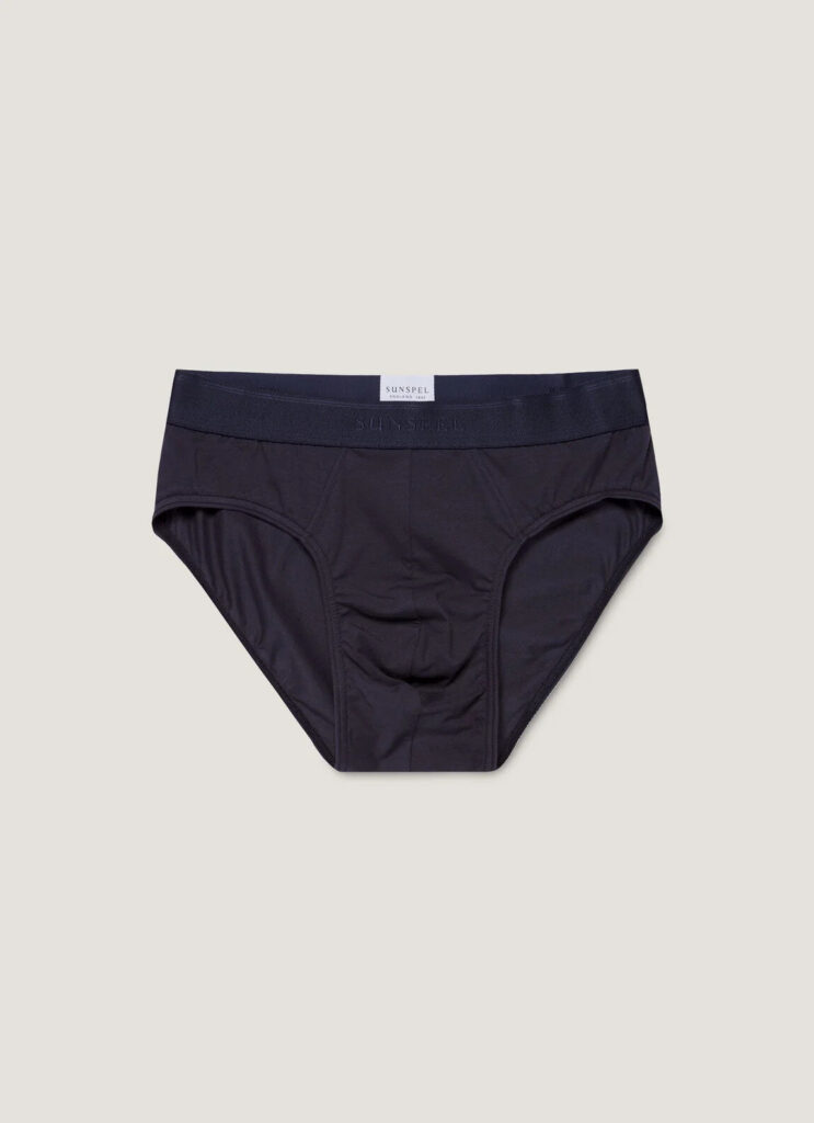 Sunspel stretch cotton brief in navy, folded on an oak surface beside a white T-shirt