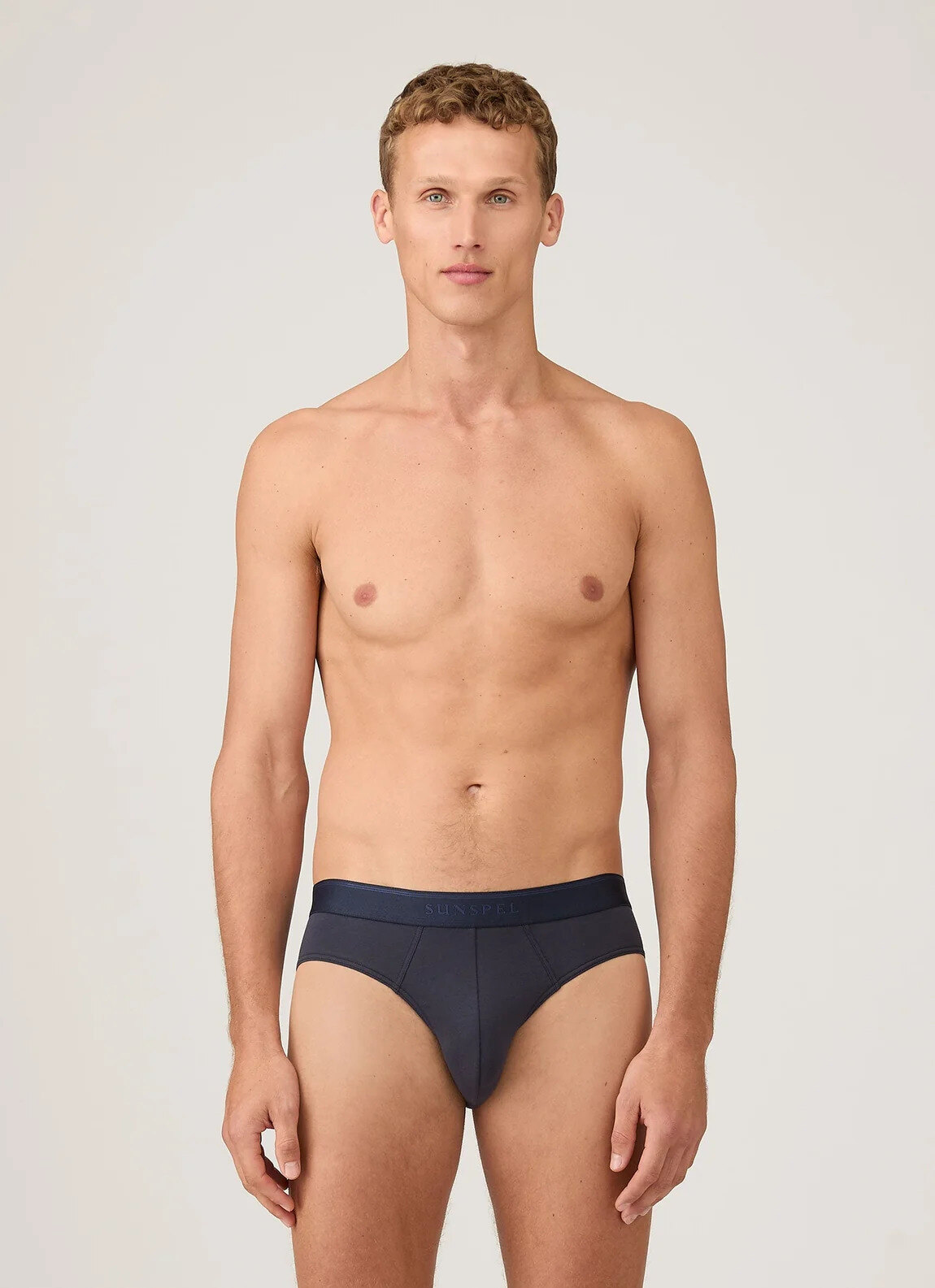 Sunspel stretch cotton brief in navy, folded on an oak surface beside a white T-shirt