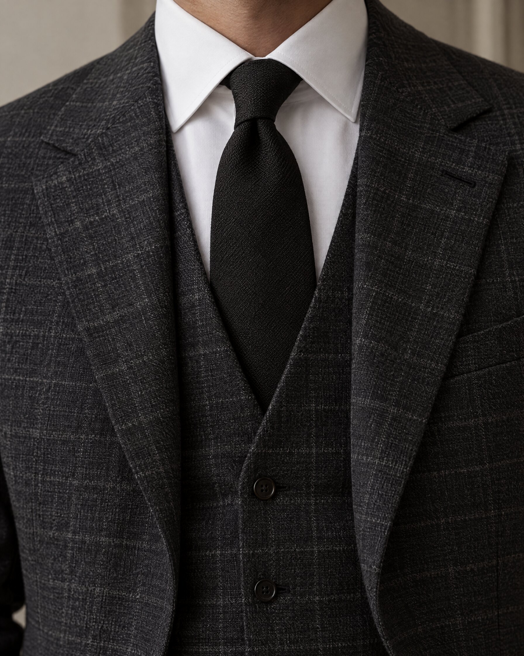 Man wearing a plain black silk tie with a white shirt and charcoal check waistcoat, cropped below the face