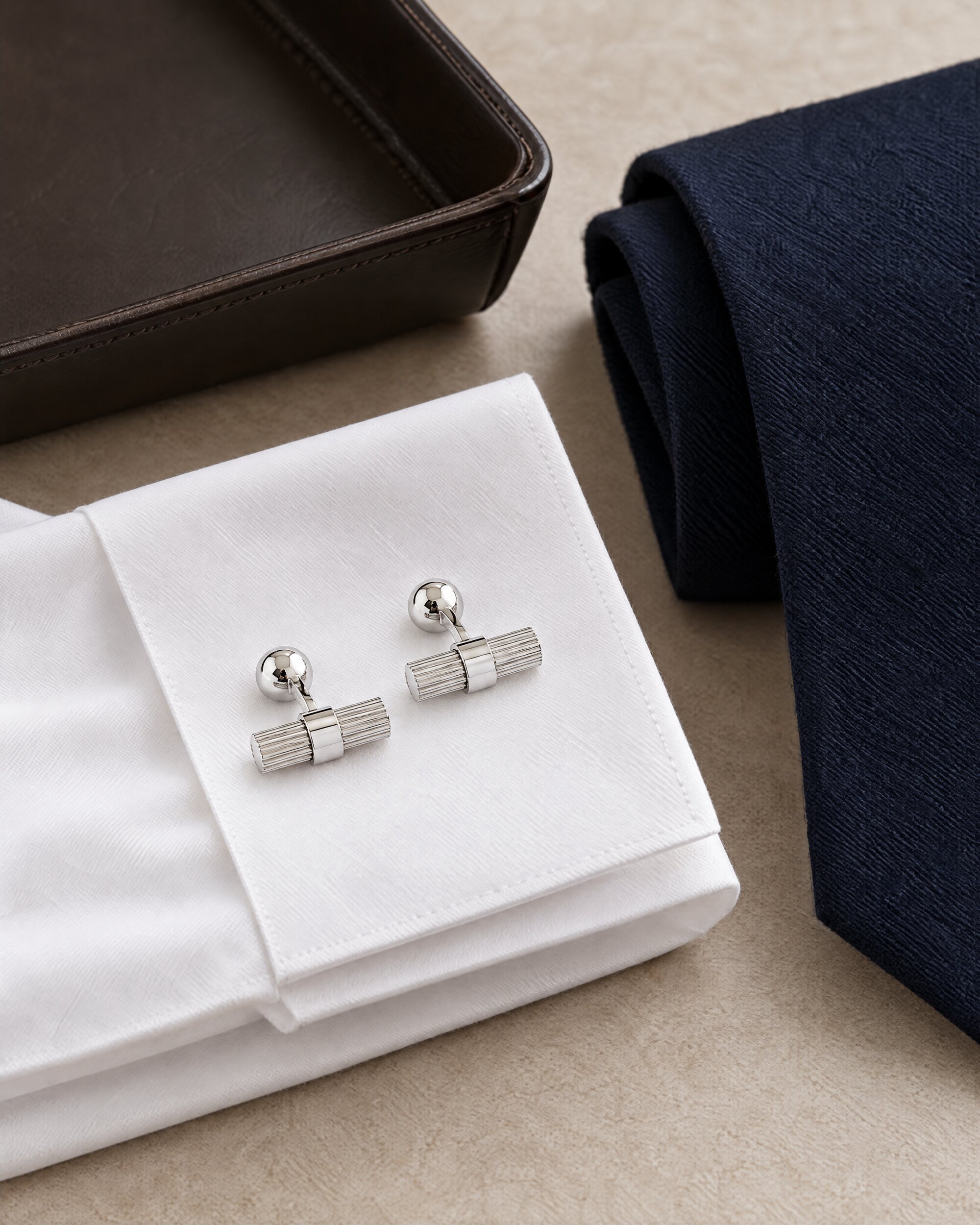 Tom Ford cylinder cufflinks in white gold on a folded white shirt cuff with a navy tie