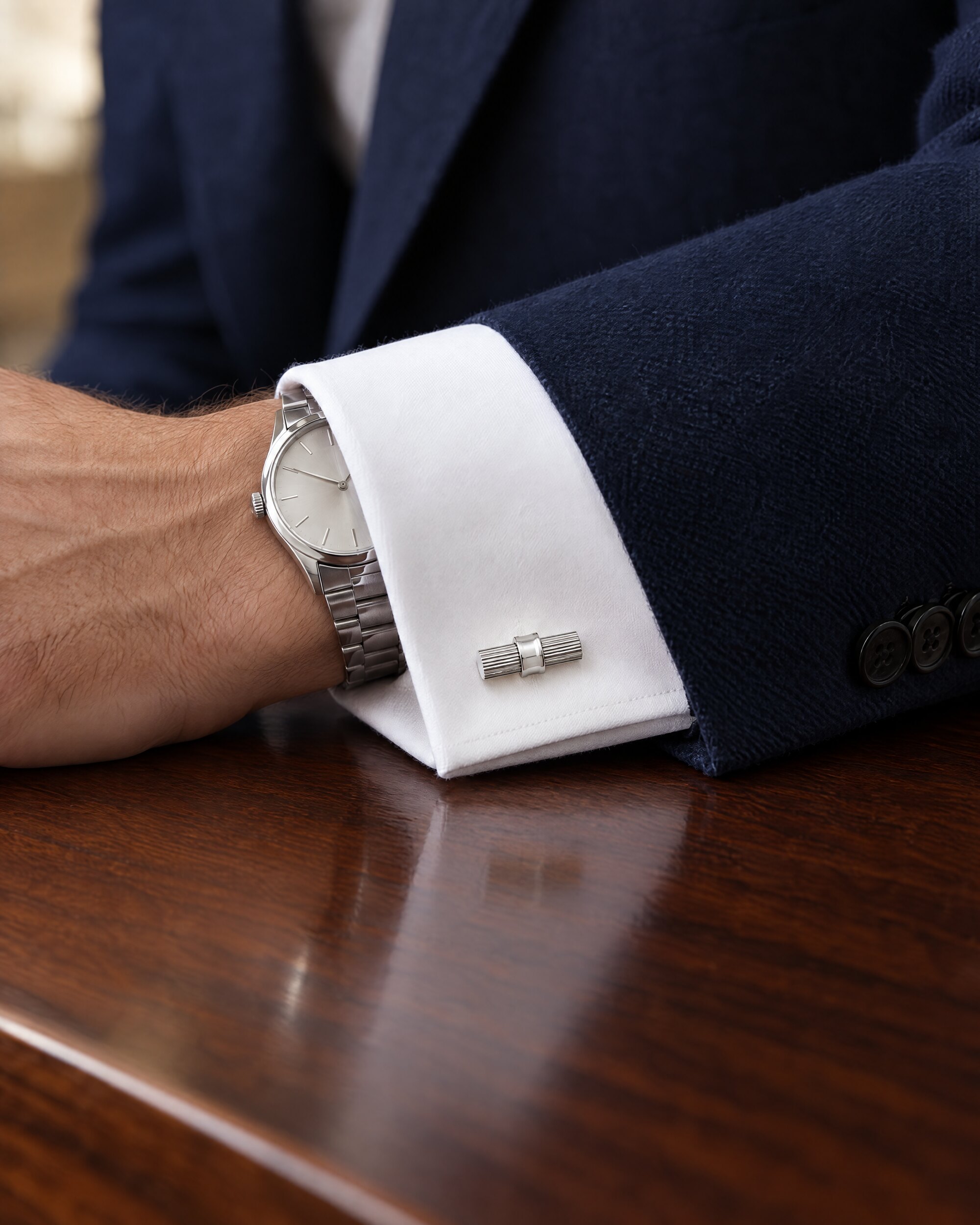White gold cylinder cufflinks fastening a white double cuff under a navy suit sleeve
