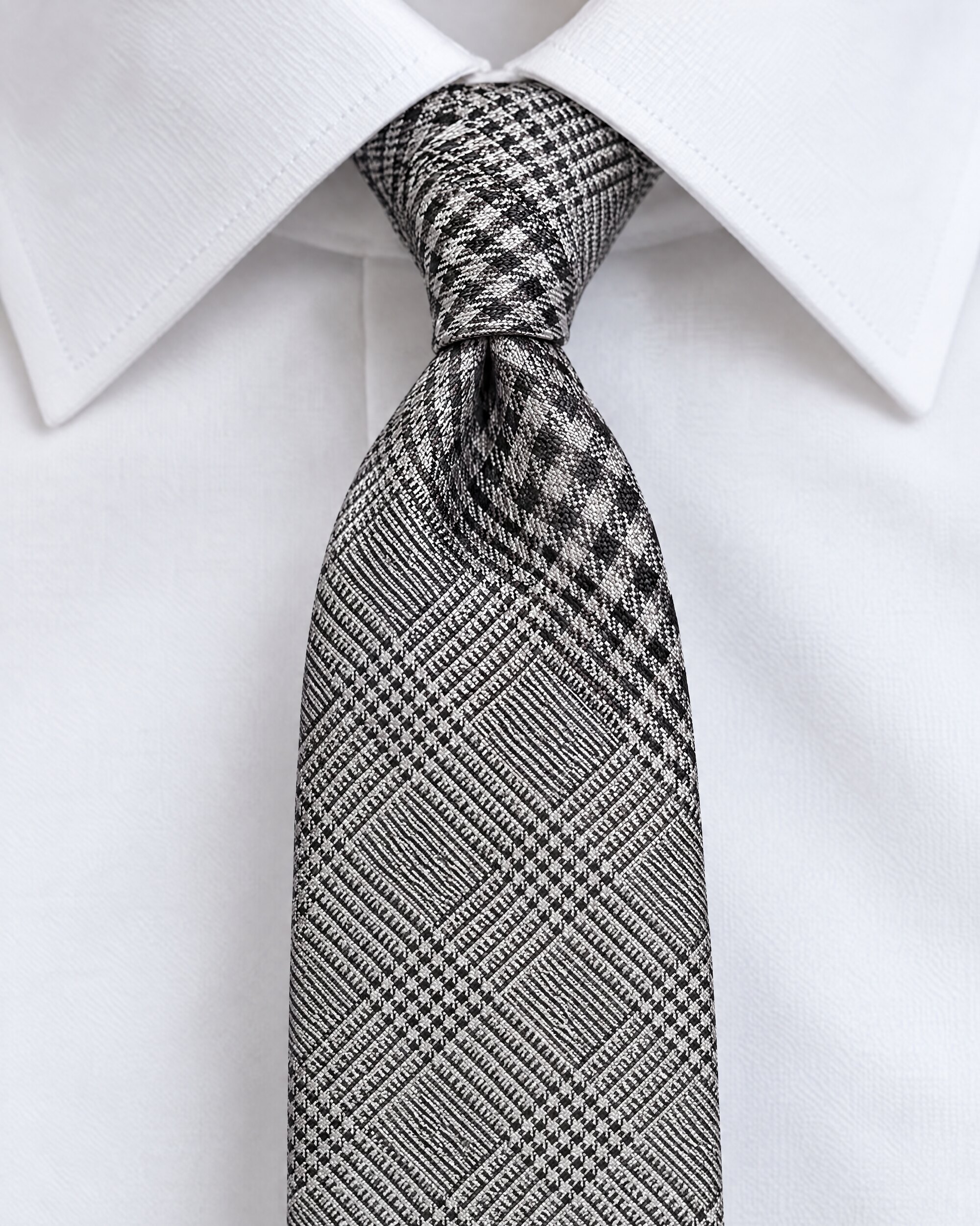 Small knot of a slim black and silver check tie under a white collar