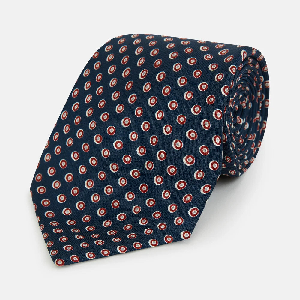 Grey silk tie with blue circles folded on a walnut table beside a white shirt